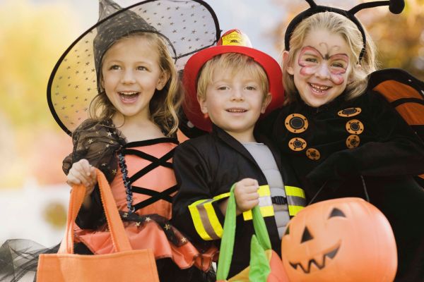 3 children dressed in halloween costumes and holding pumpkins and trick or treat bags.