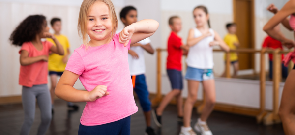 Young girl smiling while exercising with other children in the background.